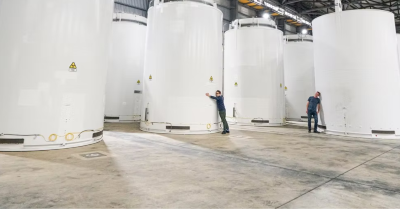 Two men interact with large casks of spent nuclear fuel